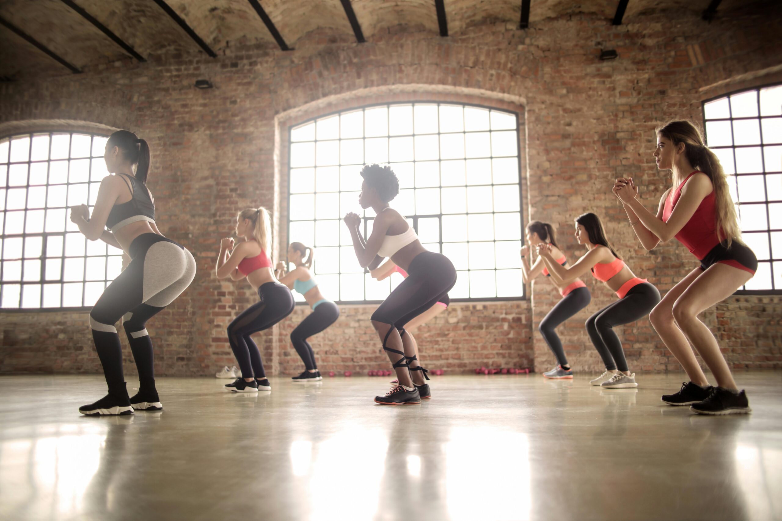 Women participating in a group fitness class performing squats in an industrial-style studio.